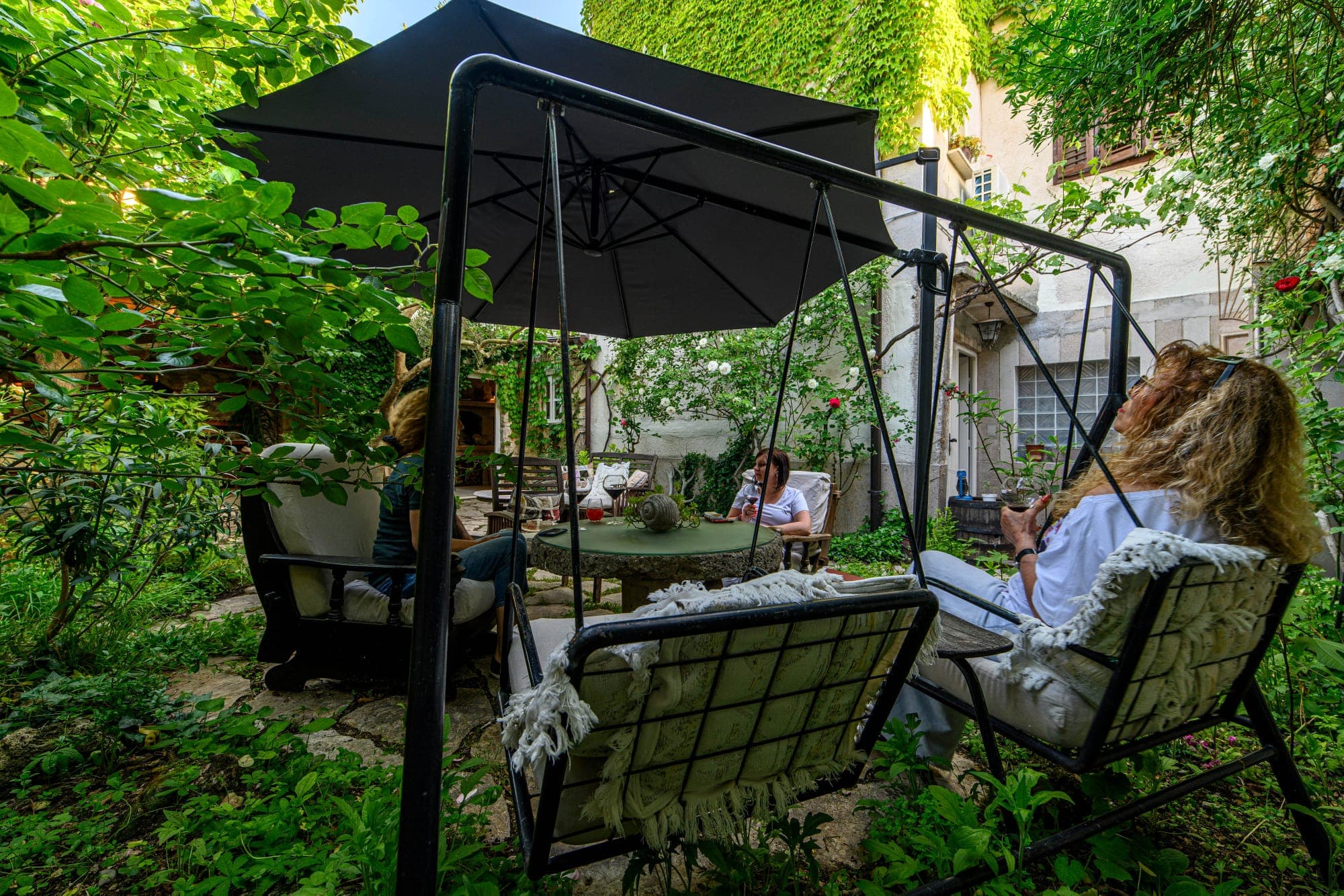 Gosti sjede za stolom u vrtu Wine Garden Skradin s čašama vina pri zalazu sunca